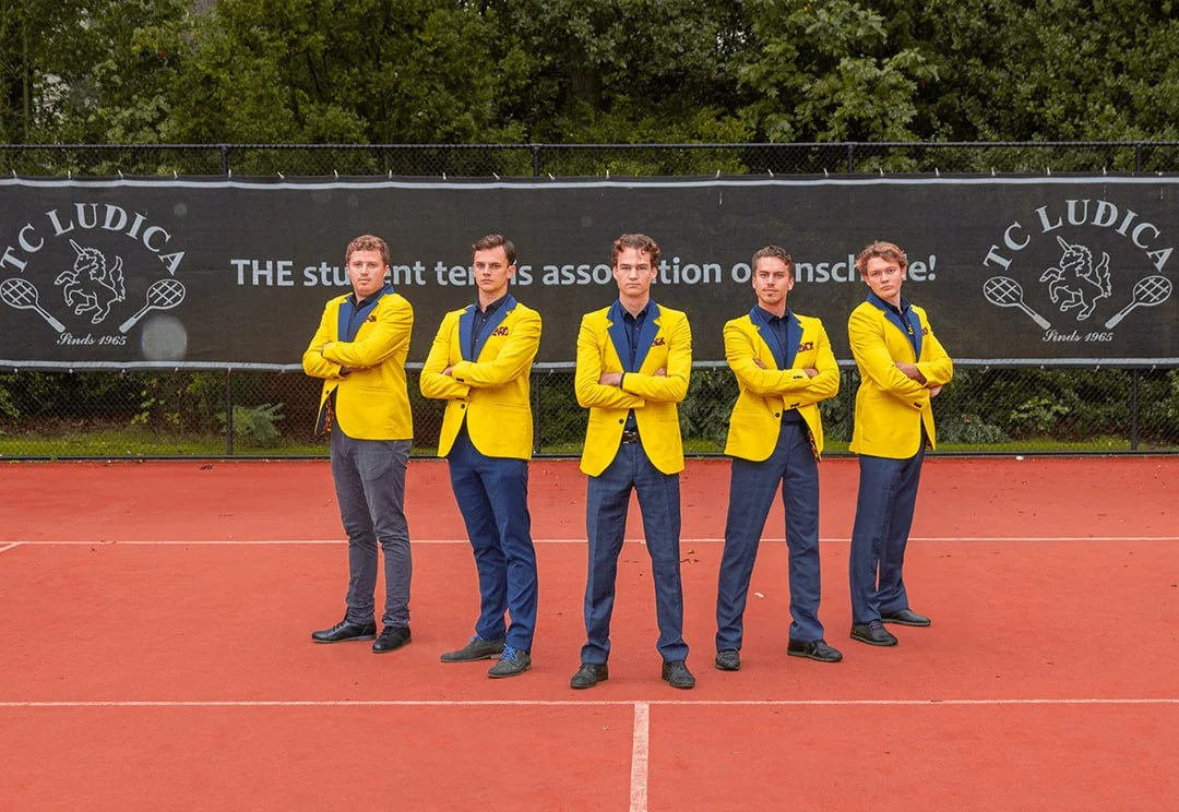 Het bestuur van T.C. Ludica in gele blazers op de tennisbaan